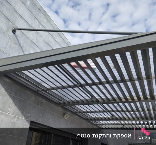 פרגולה מתכתית עם גג שקוף על קיר חיצוני